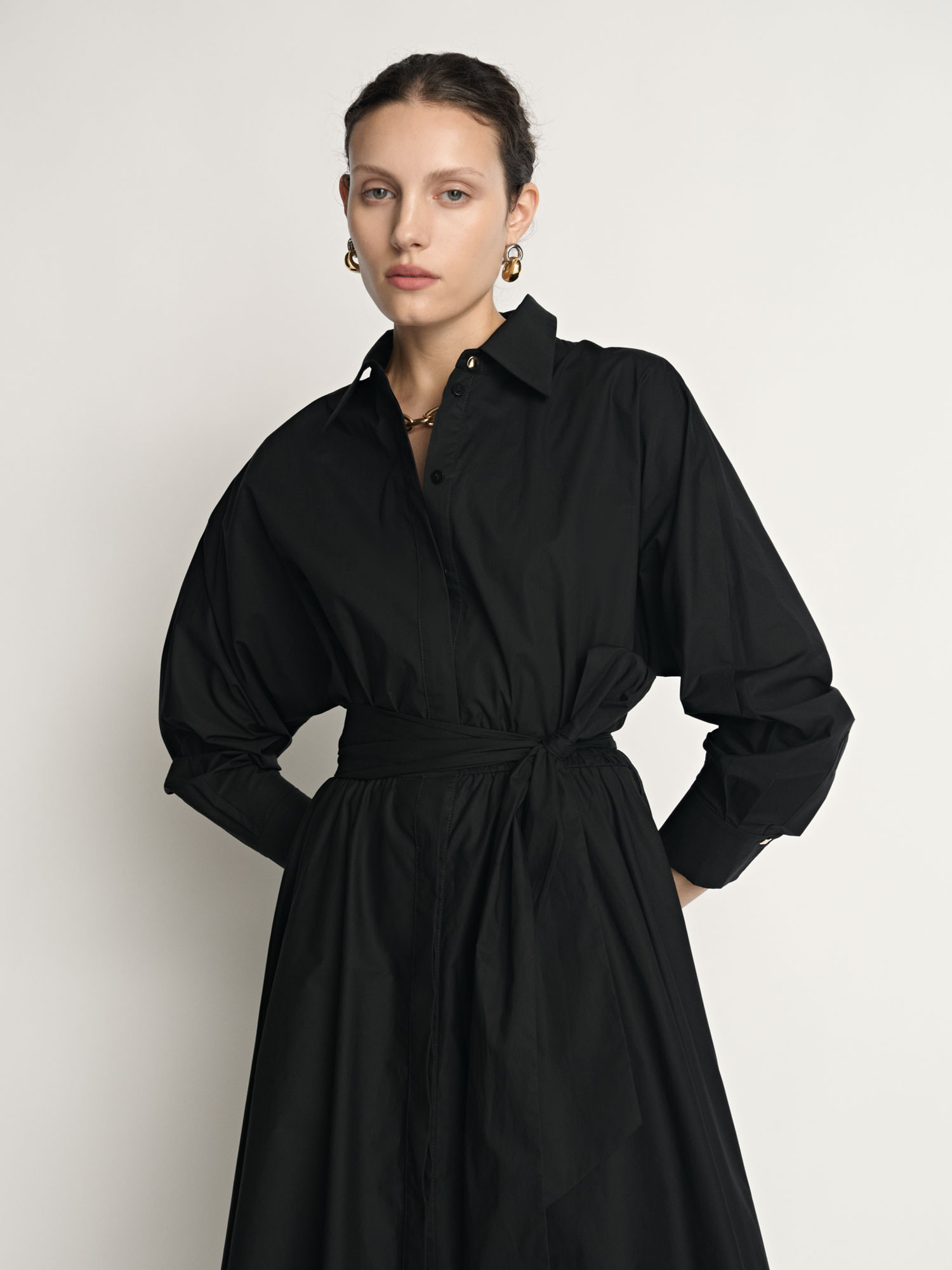 Three-quarter portrait of a model wearing a black Veronika Maine shirt dress photographed for fashion e-commerce.