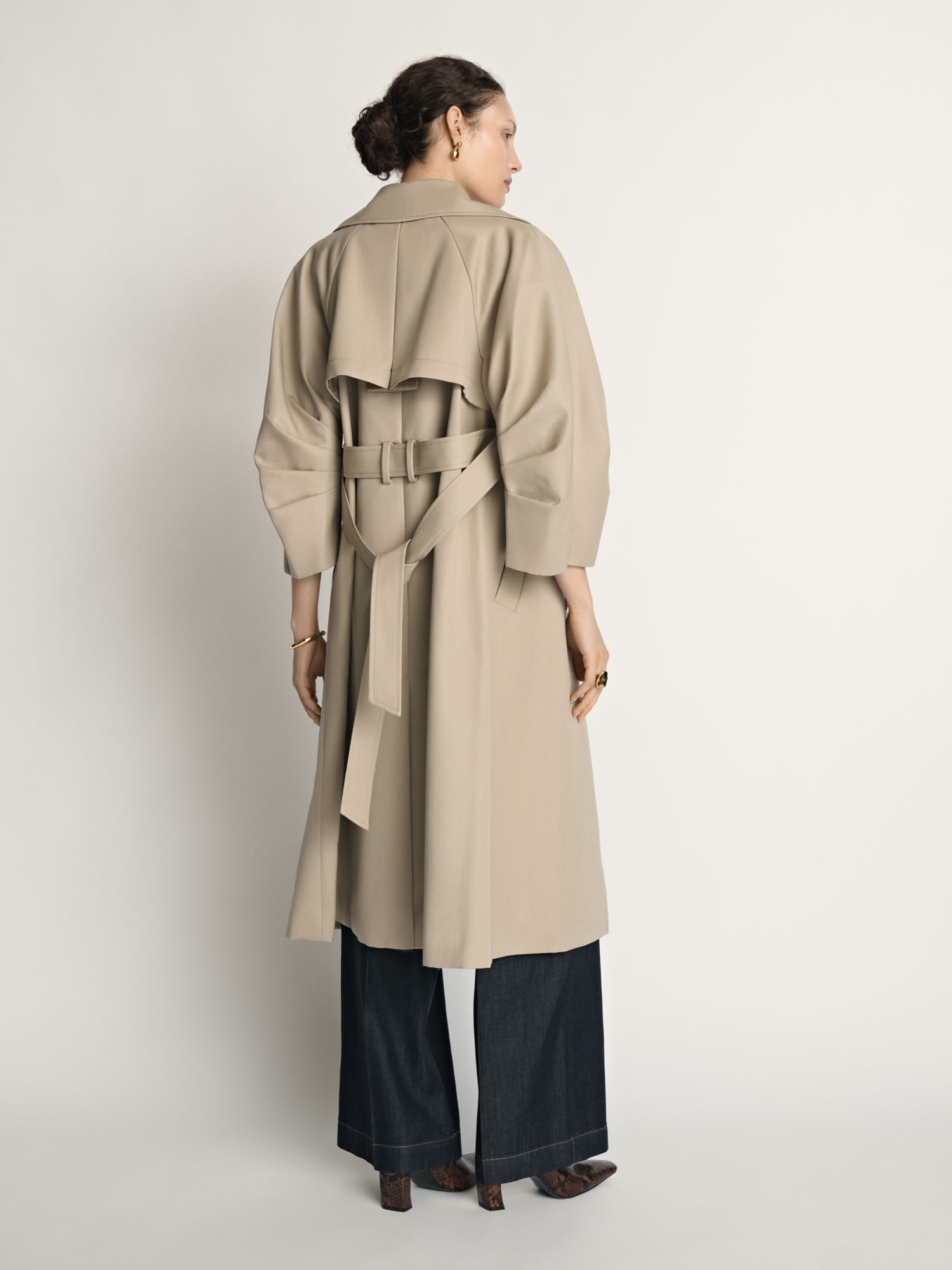 Back view of a model wearing a beige Veronika Maine trench coat photographed for fashion e-commerce.