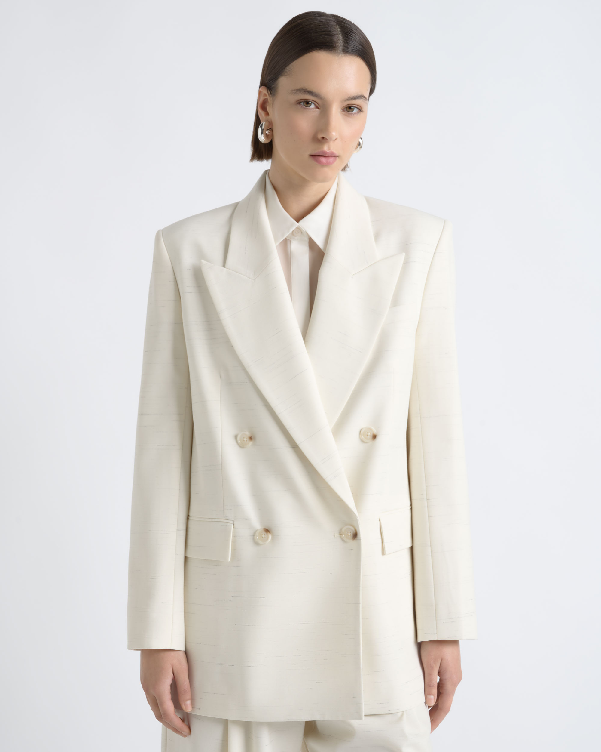 Portrait of a model wearing a CUE ivory double-breasted blazer.