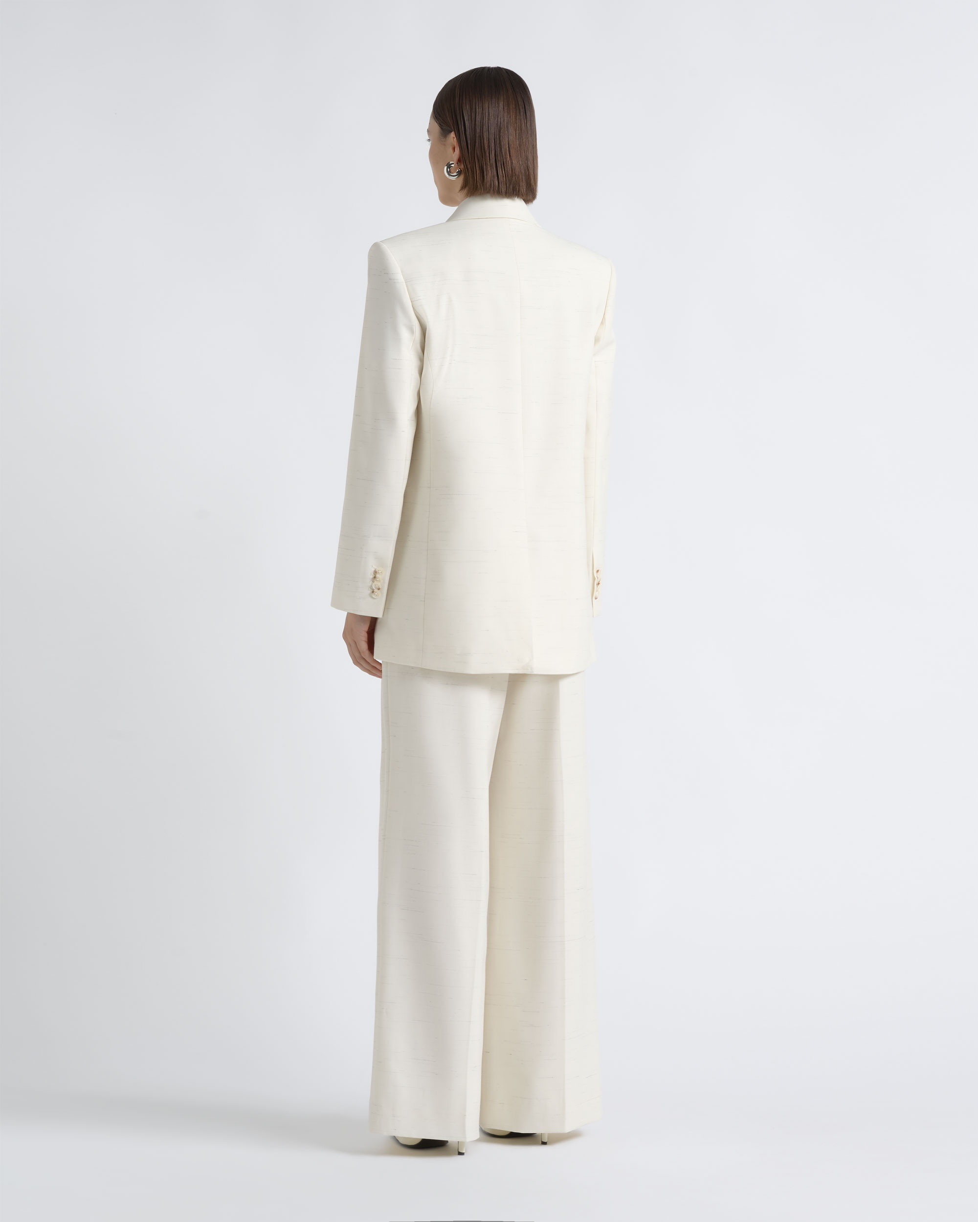 Back view of a model wearing a CUE ivory blazer and wide-leg trousers.